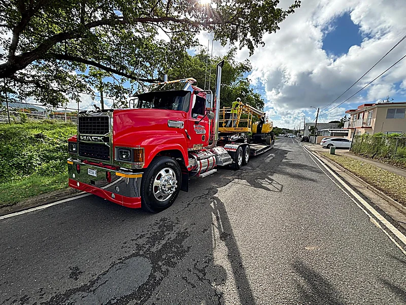 Lowboy rojo con boom lift en una calle